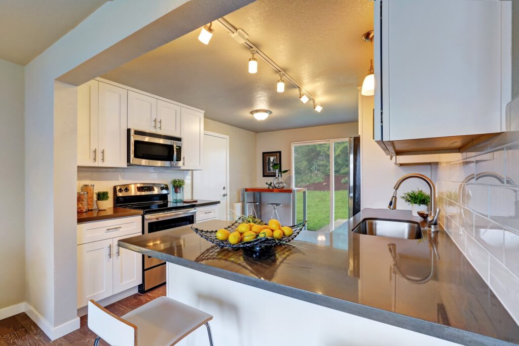 A Clean White Kitchen with a Reflective Gray Countertop with a Basket of Lemons on it and a Sliding Door at the Back