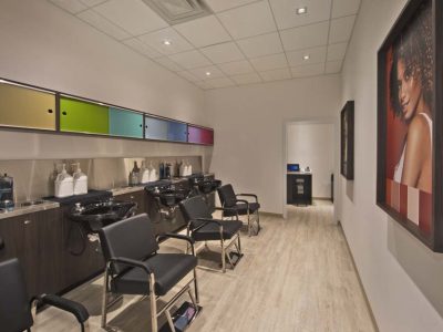 A salon with black chairs pushed again sinks, colorful cabinets, shampoo and conditioner, and a photo of a woman on a wall.