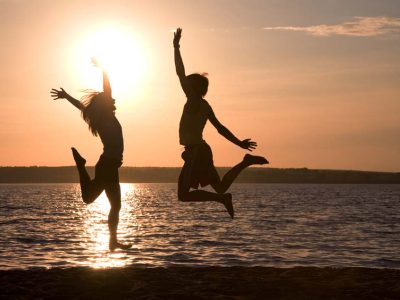 Silhouettes of happy couple jumping on background of lake at sunset